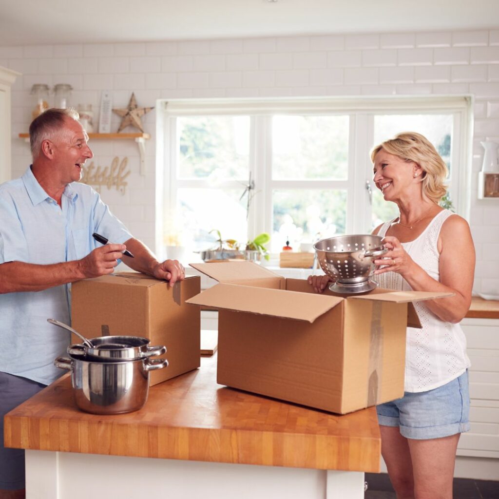 A couple unpacking kitchen items and smiling in a bright home.