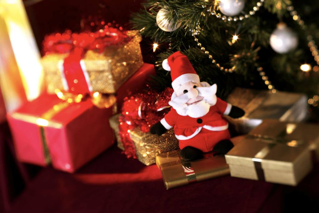 A festive display with a plush santa claus toy, wrapped gifts, and christmas decorations under a tree.