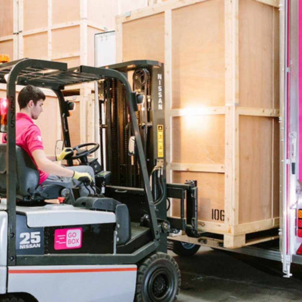 A worker operating a forklift to move a large wooden crate into a truck.