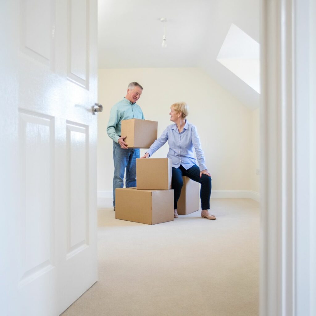 Couple unpacking boxes in a bright, empty room after downsizing.