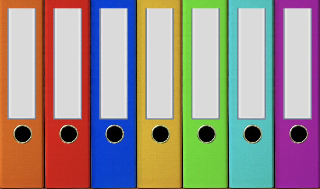 A row of colorful office binders with blank labels on a shelf.