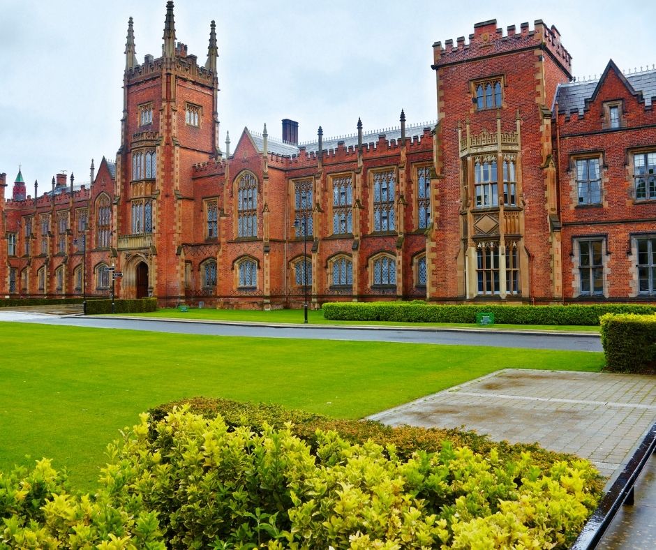 Gothic revival architecture of a historic university building with manicured lawns and hedges in the foreground.
