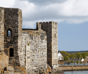 An ancient stone fortress with a robust wall facing a body of water under a partly cloudy sky.