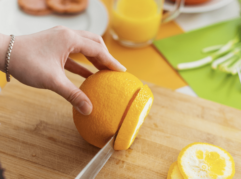 A person slicing an orange on a wooden cutting board.