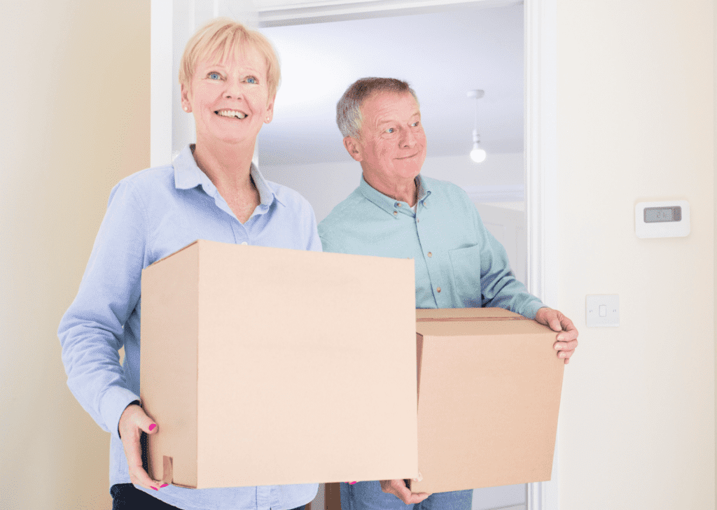 A smiling senior couple holding cardboard boxes, possibly moving into a new home.