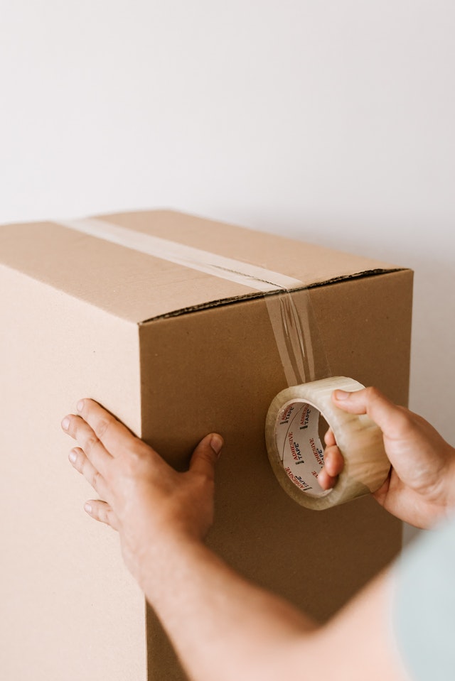 A person securing a cardboard box with packing tape.