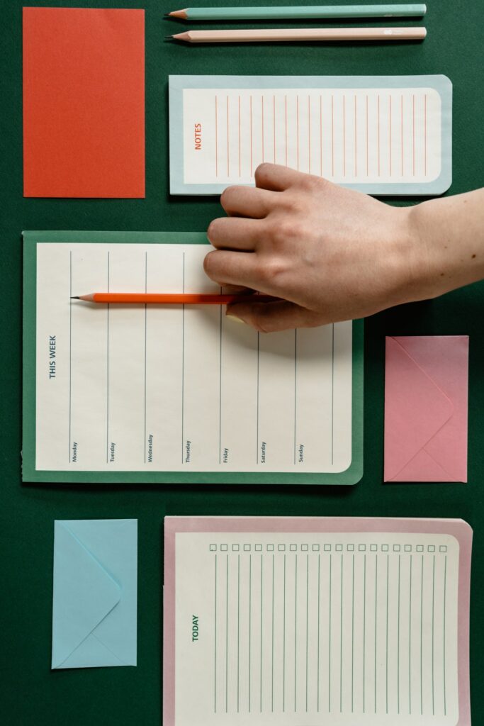 A person organizing stationery items on a green surface, including planners and envelopes.