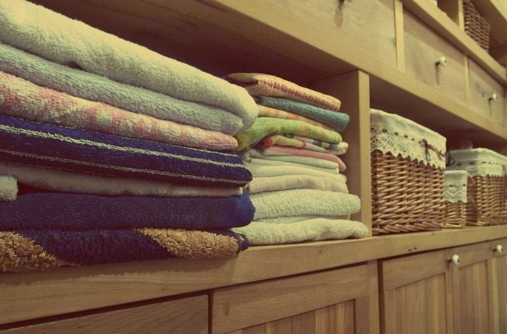 Neatly folded towels on a wooden shelf next to wicker baskets.