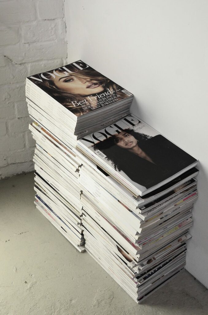 Stack of assorted magazines piled in a corner against a white wall, an essential way to successfully sell your home.